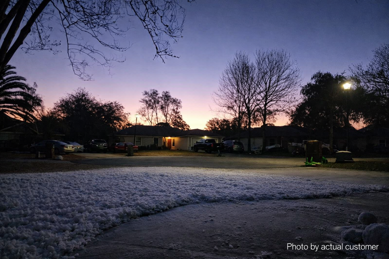 Snow-covered yard at dusk with warm house lights in the background